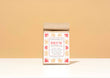 A kraft paper bag of Harbor Herbalist Brew Decaf Herbal Chai tea stands centered on a white surface against a warm beige background. The packaging features red and gold botanical illustrations.