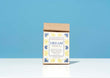 A kraft paper bag of Harbor Herbalist Dream Nighttime Tea stands upright on a white surface against a solid blue background. The packaging features a white front label with blue and yellow botanical illustrations.