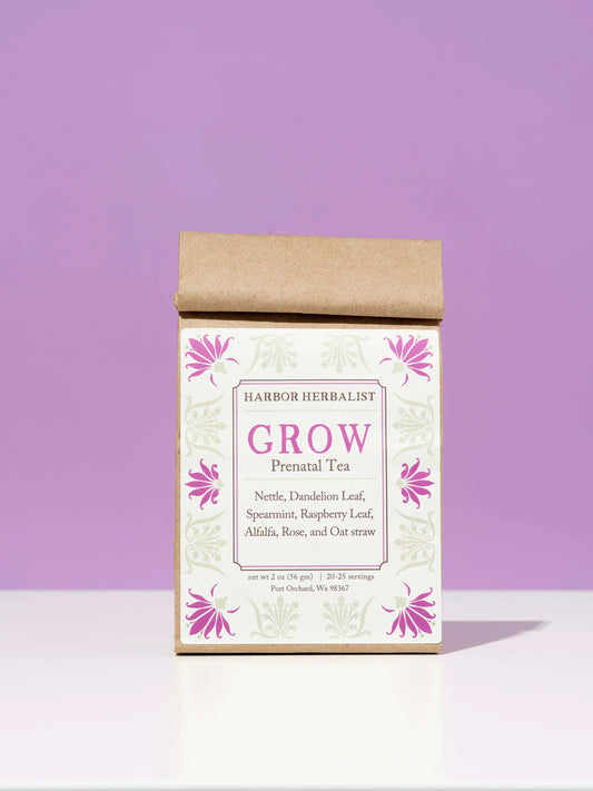 A kraft paper bag of Harbor Herbalist 'Grow' Prenatal Tea, featuring a white front label with pink floral illustrations, set against a solid lavender background on a white surface.