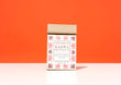 A kraft paper bag of Harbor Herbalist Kahwa Kashmiri Inspired Tea stands upright on a white surface against a solid orange background. The bag features a white front label with red botanical illustrations and black text.