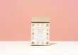 A kraft paper bag of Harbor Herbalist Kukicha Gold Loose Leaf Tea, featuring a white label and copper-gold botanical illustrations, set against a solid pink background on a white surface.