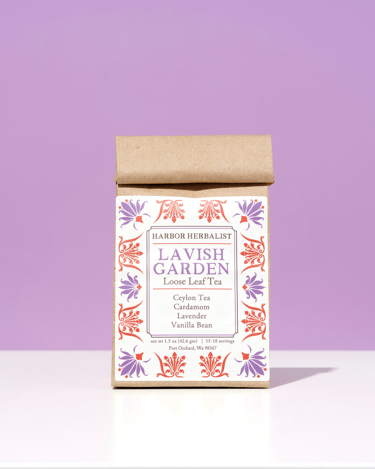 A bag of Harbor Herbalist Lavish Garden loose leaf herbal tea, featuring a white label decorated with red and purple botanical illustrations, set against a solid lavender background on a white surface.