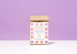 A bag of Harbor Herbalist Lavish Garden loose leaf herbal tea, featuring a white label decorated with red and purple botanical illustrations, set against a solid lavender background on a white surface.