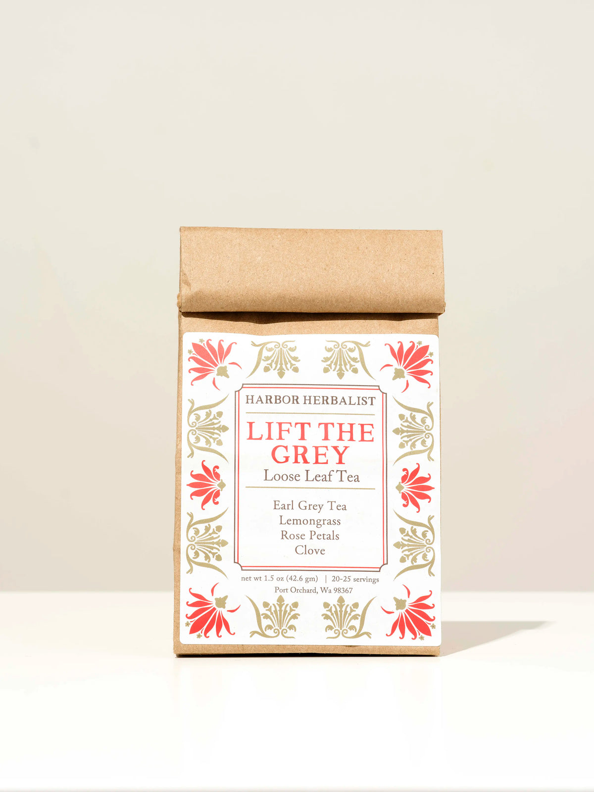 A kraft paper bag of Harbor Herbalist Lift The Grey Loose Leaf Tea, featuring a white label with red and gold botanical illustrations, set against a plain off-white background.