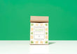 A bag of Harbor Herbalist Maghreb Moroccan Mint loose leaf tea, featuring a white label decorated with green and yellow botanical illustrations, stands on a white surface against a vibrant green background.
