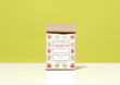 A kraft paper bag of Harbor Herbalist Strength Loose Leaf Tea stands upright on a white surface against a solid yellow-green background. The kraft paper box has a white label decorated with pink and gold botanical illustrations.