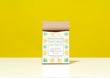 A kraft paper bag of Harbor Herbalist Wellness Immune Support Tea stands on a white surface against a bright yellow background. The packaging features a white label with green and gold botanical illustrations and teal text.
