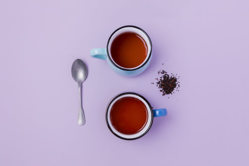 Two cups of organic tea on a lavender colored background